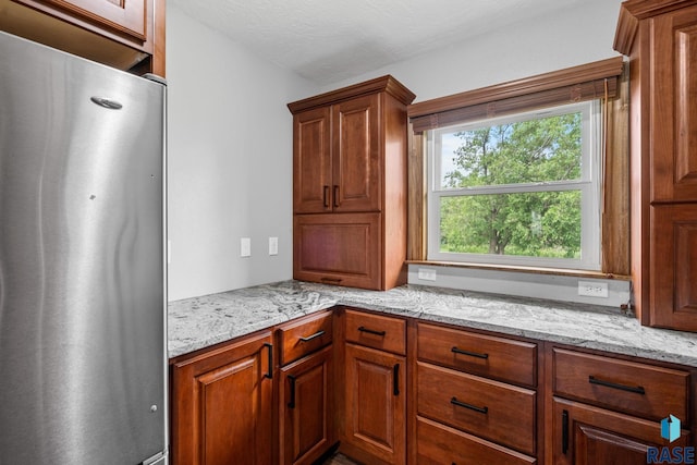 kitchen featuring a textured ceiling, light stone counters, and stainless steel refrigerator