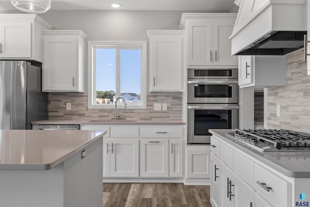 kitchen with appliances with stainless steel finishes, backsplash, custom exhaust hood, white cabinets, and light hardwood / wood-style flooring