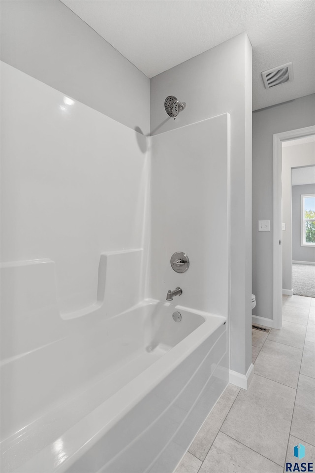 bathroom featuring toilet, shower / bathing tub combination, tile patterned floors, and a textured ceiling