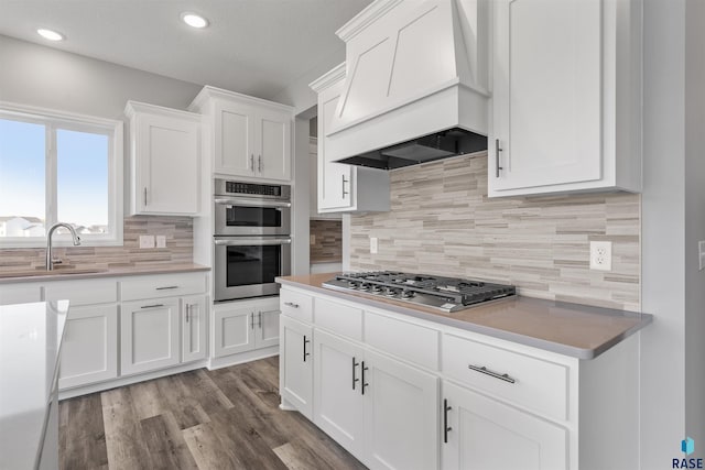 kitchen featuring white cabinets, backsplash, appliances with stainless steel finishes, custom range hood, and light hardwood / wood-style floors