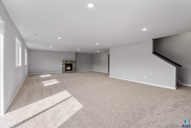 unfurnished living room with a stone fireplace and light colored carpet