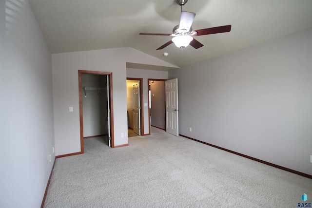 unfurnished bedroom featuring light carpet, ceiling fan, vaulted ceiling, a closet, and a walk in closet