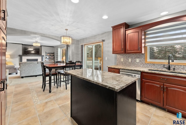 kitchen featuring light stone countertops, sink, dishwasher, a kitchen island, and hanging light fixtures