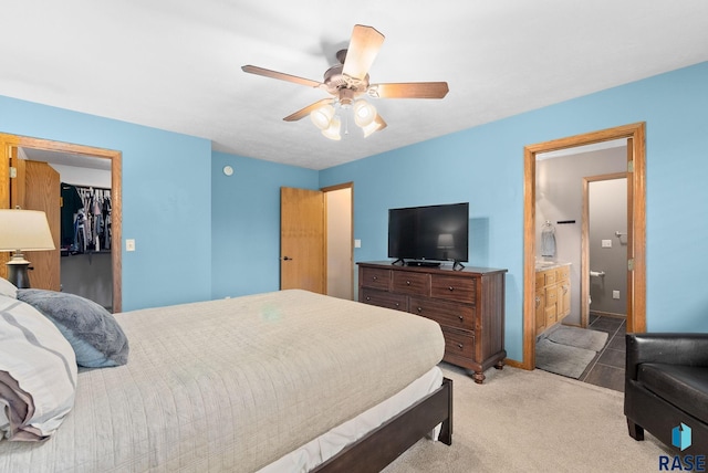 bedroom featuring a closet, light carpet, a walk in closet, ensuite bathroom, and ceiling fan