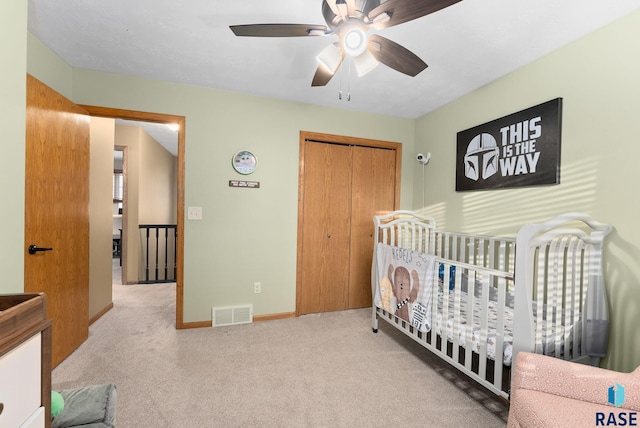 bedroom featuring a nursery area, light colored carpet, a closet, and ceiling fan