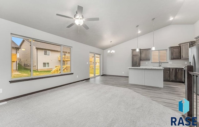 unfurnished living room featuring light colored carpet, sink, ceiling fan with notable chandelier, and vaulted ceiling