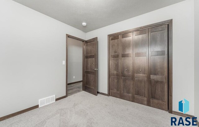 unfurnished bedroom featuring light carpet, a closet, and a textured ceiling