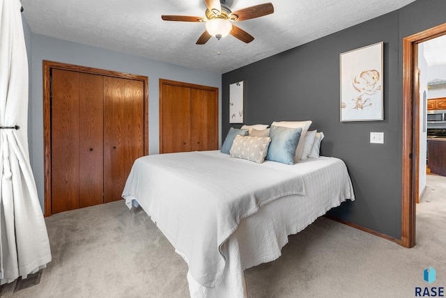 bedroom featuring ceiling fan, multiple closets, a textured ceiling, and light colored carpet