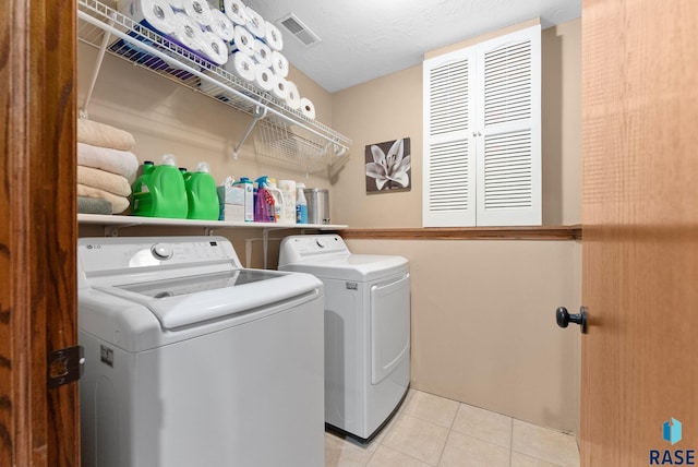 washroom with a textured ceiling, washing machine and dryer, and light tile patterned floors