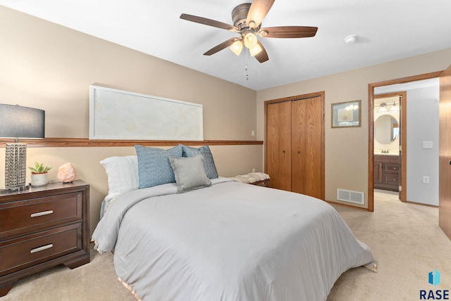 bedroom with a closet, ceiling fan, light carpet, and ensuite bath