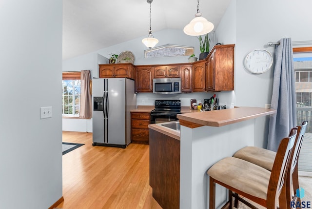 kitchen with light wood-type flooring, stainless steel appliances, vaulted ceiling, decorative light fixtures, and a breakfast bar area