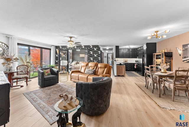 living room with light hardwood / wood-style flooring, a textured ceiling, and ceiling fan with notable chandelier