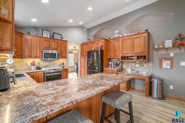 kitchen with appliances with stainless steel finishes, a kitchen bar, kitchen peninsula, lofted ceiling, and light hardwood / wood-style flooring