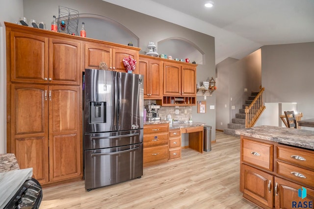 kitchen with light stone countertops, light wood-type flooring, vaulted ceiling, decorative backsplash, and stainless steel refrigerator with ice dispenser