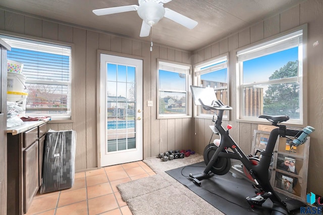 workout room with ceiling fan, light tile patterned floors, and wooden walls