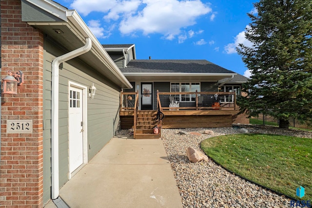 view of exterior entry with a wooden deck and a lawn