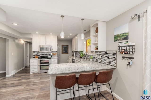 kitchen with stainless steel appliances, white cabinetry, kitchen peninsula, tasteful backsplash, and light wood-type flooring