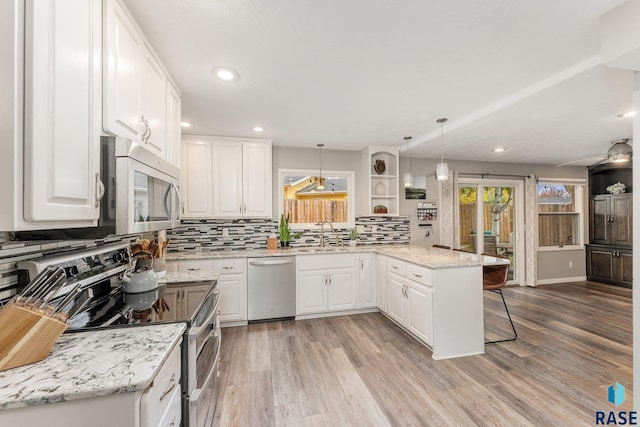 kitchen with stainless steel appliances, white cabinets, kitchen peninsula, a kitchen breakfast bar, and pendant lighting