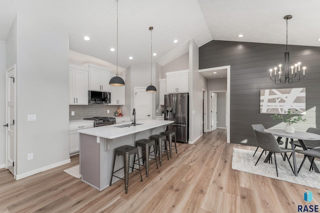 kitchen featuring appliances with stainless steel finishes, pendant lighting, sink, white cabinets, and a kitchen island with sink