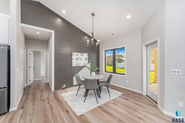 dining area featuring high vaulted ceiling, a notable chandelier, wooden walls, and light hardwood / wood-style flooring