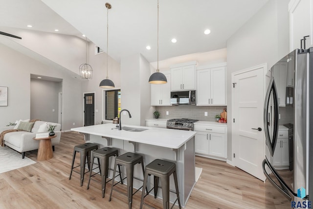 kitchen featuring appliances with stainless steel finishes, decorative light fixtures, sink, white cabinets, and a kitchen island with sink