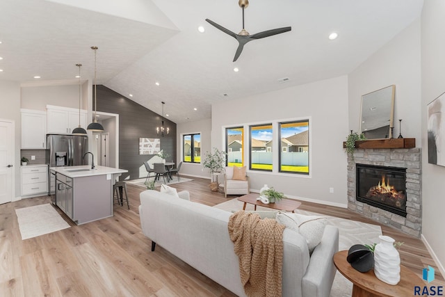 living room featuring sink, high vaulted ceiling, light hardwood / wood-style flooring, a fireplace, and ceiling fan with notable chandelier