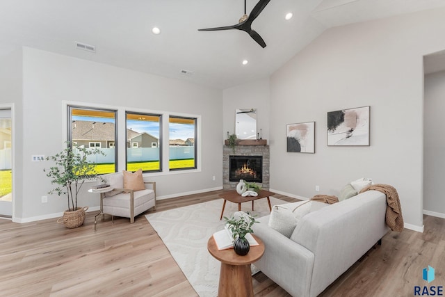 living room with ceiling fan, lofted ceiling, a stone fireplace, and light hardwood / wood-style floors