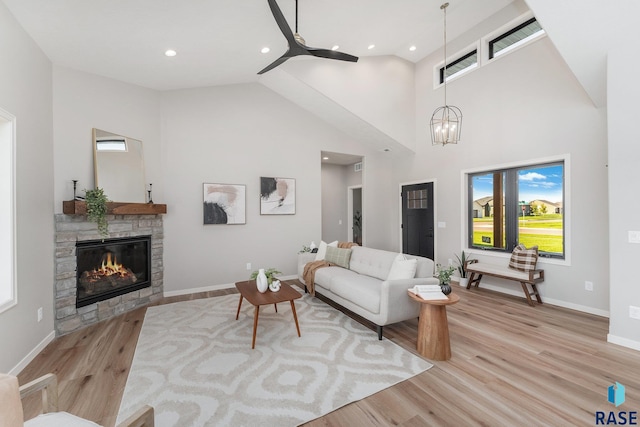 living room featuring light hardwood / wood-style flooring, a fireplace, high vaulted ceiling, and ceiling fan