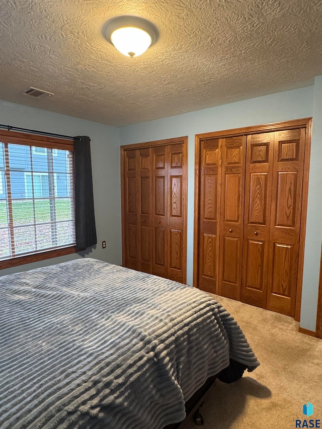 carpeted bedroom with multiple closets and a textured ceiling