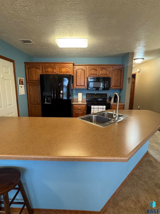 kitchen with black appliances, sink, a breakfast bar area, and a textured ceiling