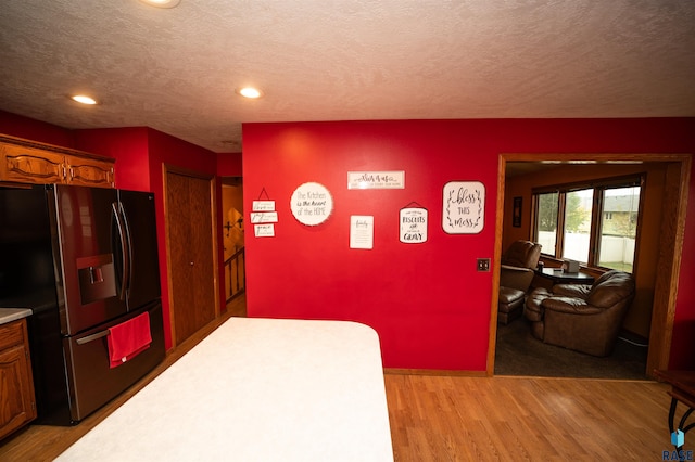 kitchen with light wood-style flooring, a textured ceiling, light countertops, and fridge with ice dispenser