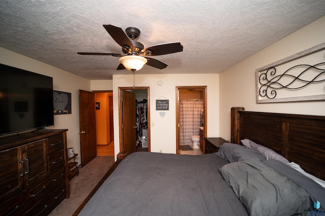 carpeted bedroom with a walk in closet, a closet, a textured ceiling, ensuite bath, and a ceiling fan