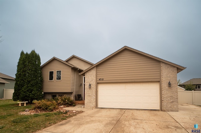 split level home featuring brick siding, an attached garage, concrete driveway, and fence