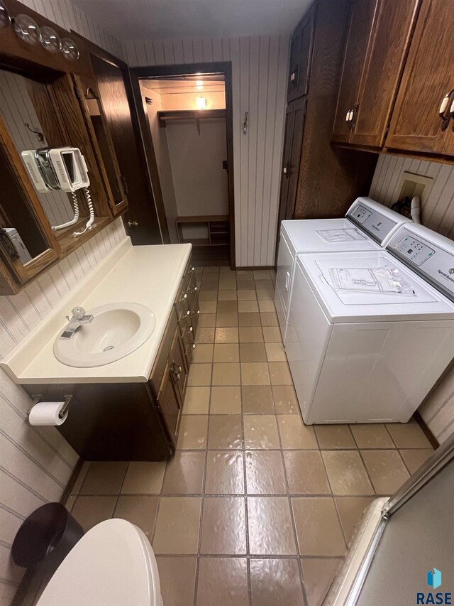 laundry area with light tile patterned flooring, wood walls, sink, and washer and dryer