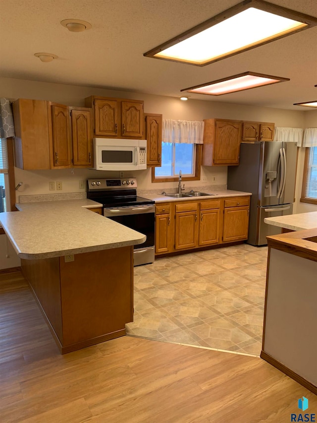 kitchen with kitchen peninsula, sink, light wood-type flooring, and appliances with stainless steel finishes