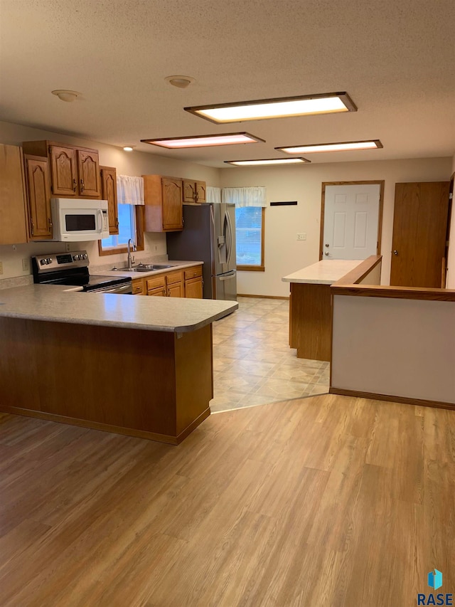 kitchen with light wood-type flooring, kitchen peninsula, a textured ceiling, and stainless steel appliances