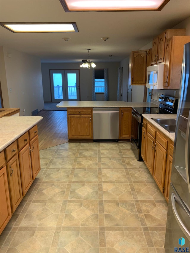 kitchen with kitchen peninsula, stainless steel appliances, a notable chandelier, and light hardwood / wood-style floors