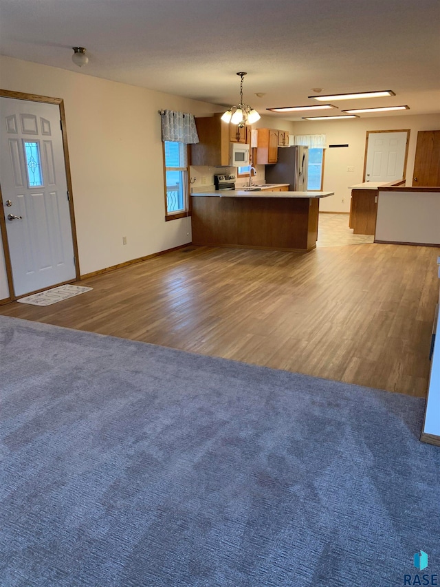 kitchen featuring kitchen peninsula, sink, light wood-type flooring, appliances with stainless steel finishes, and decorative light fixtures