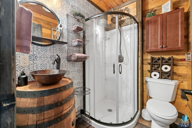 bathroom featuring wood walls, sink, a shower with door, and toilet