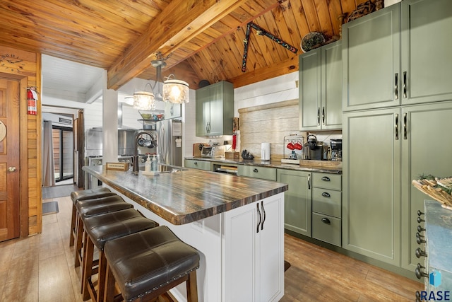 kitchen featuring beam ceiling, hanging light fixtures, light hardwood / wood-style flooring, an island with sink, and green cabinetry