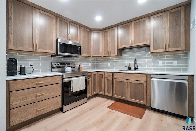 kitchen with stainless steel appliances, sink, tasteful backsplash, and light hardwood / wood-style flooring