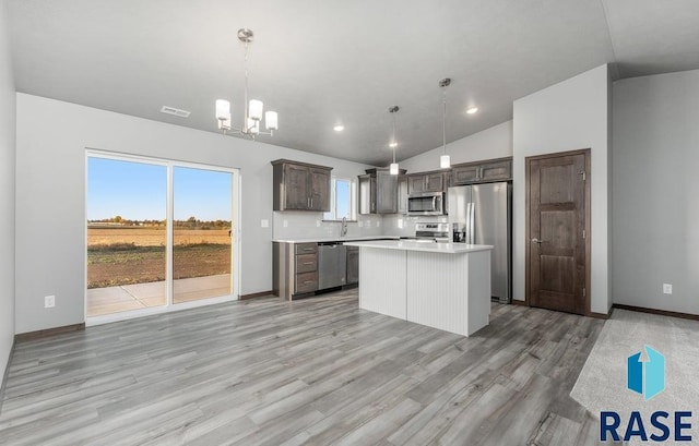 kitchen with appliances with stainless steel finishes, vaulted ceiling, decorative light fixtures, and a kitchen island