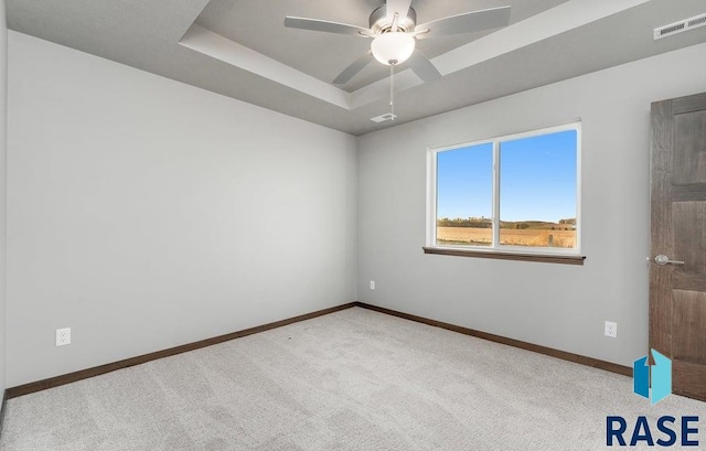 carpeted spare room with ceiling fan and a raised ceiling