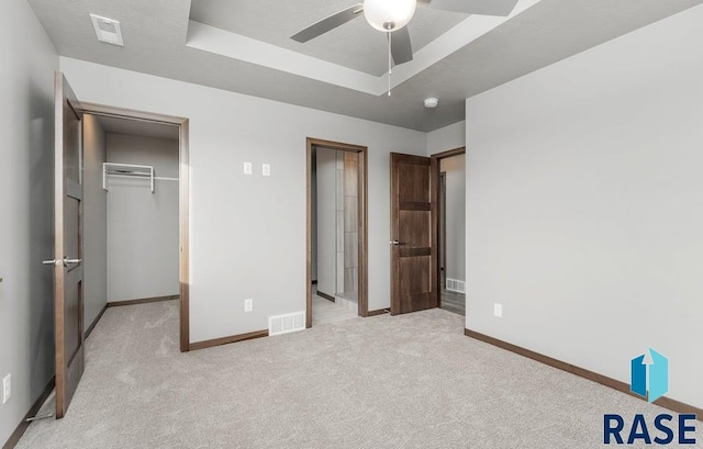 unfurnished bedroom with light colored carpet, ceiling fan, a raised ceiling, and a closet