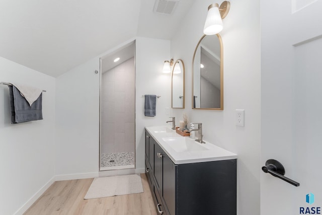 bathroom featuring vanity, vaulted ceiling, a tile shower, and wood-type flooring