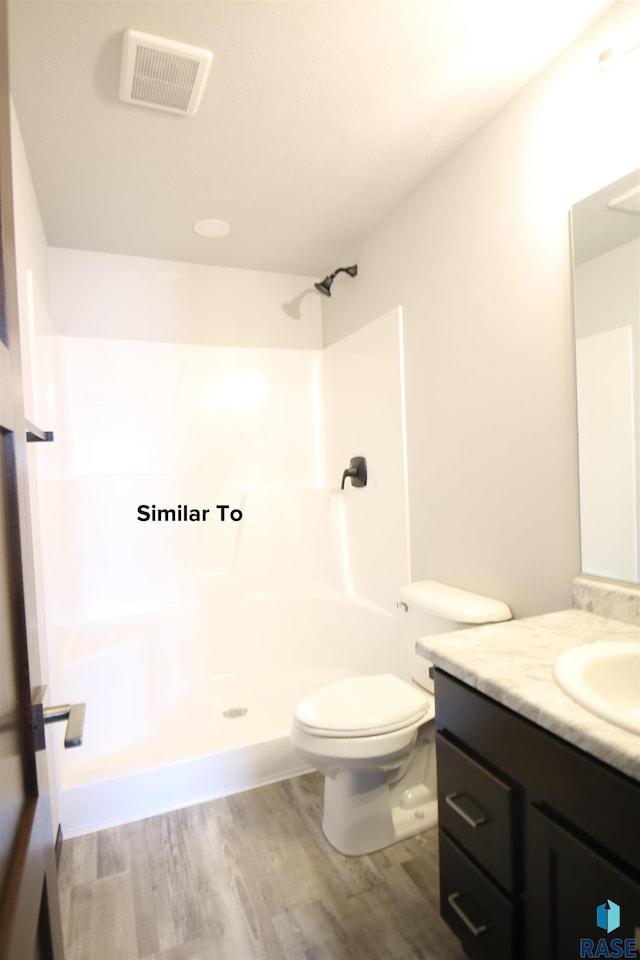 bathroom with hardwood / wood-style flooring, toilet, vanity, and walk in shower