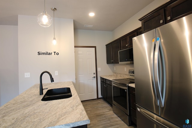 kitchen featuring stainless steel appliances, hanging light fixtures, light stone countertops, light hardwood / wood-style flooring, and sink