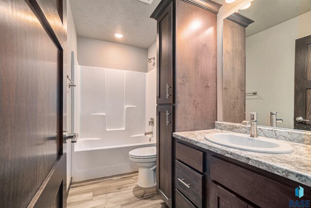 full bathroom with toilet, hardwood / wood-style floors, a textured ceiling, vanity, and bathing tub / shower combination