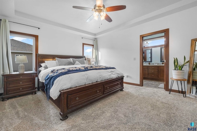 carpeted bedroom featuring ensuite bathroom, ceiling fan, and a tray ceiling