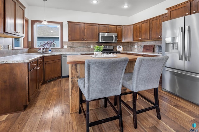 kitchen featuring stainless steel appliances, tasteful backsplash, dark hardwood / wood-style floors, a kitchen island, and decorative light fixtures